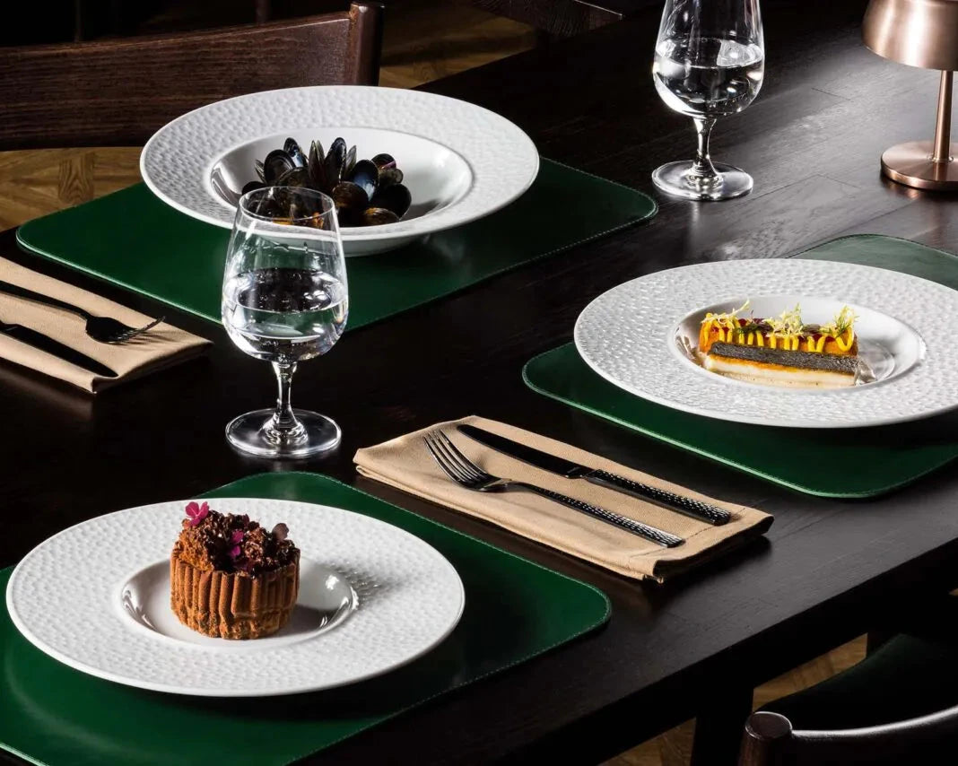 Dining table set with plates, glasses, and desserts on a dark surface.